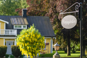 Färgbild på ett gult hus med gröna buskar runt om kring och en skylt i förgrunden med texten Finjagården